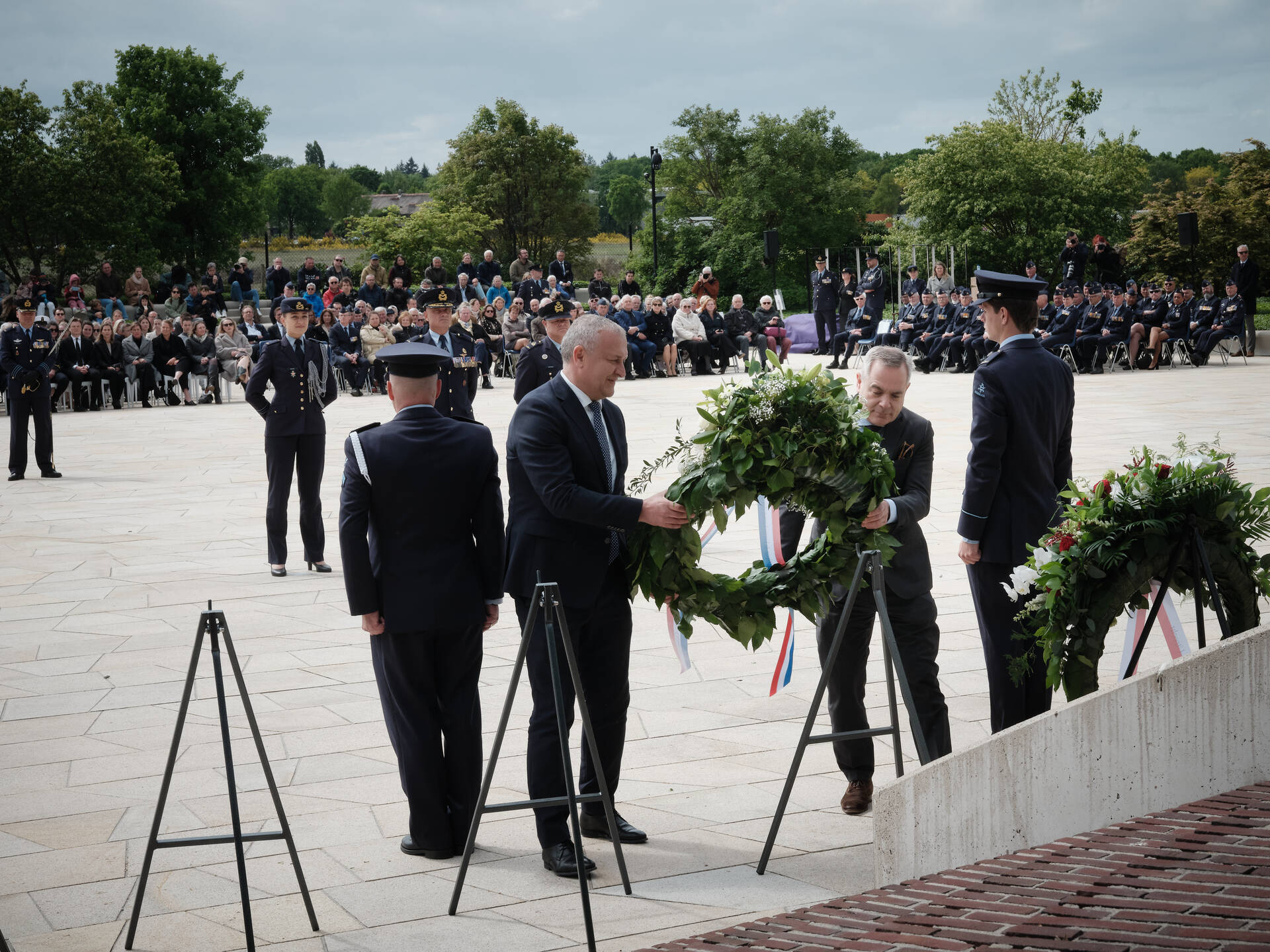 Twee mannen leggen een krans buiten bij een monument